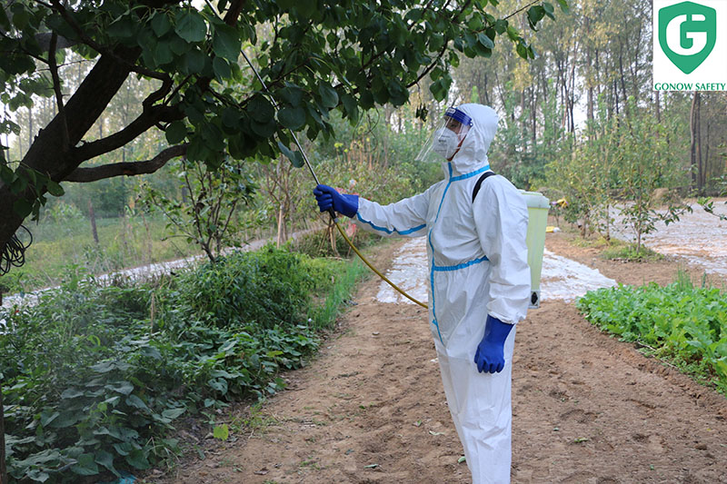 A worker wearing a Type 5/6 protective suit with adhesive strips, spraying pesticides in a field, ensuring safety against liquid splashes and particles.