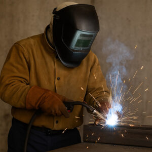Welders wearing full protective gear including helmets, gloves, and reflective clothing performing welding operations.